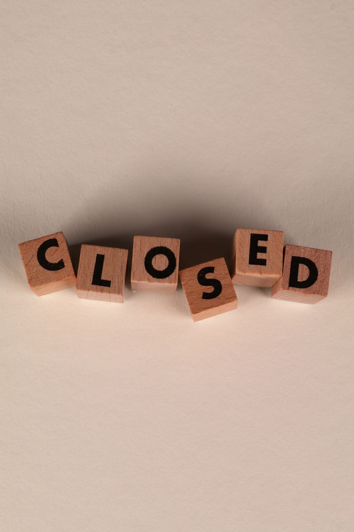 Wooden blocks arranged to spell 'CLOSED' on a beige background, conveying closure.