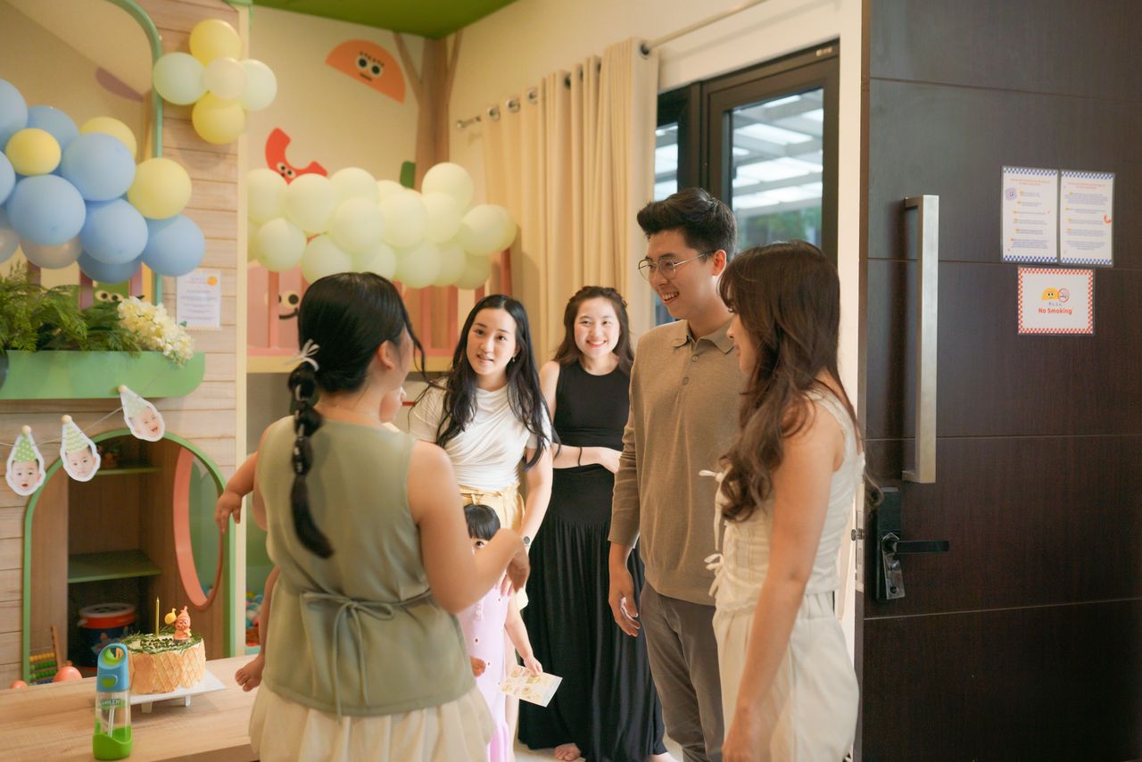 A joyful indoor birthday party featuring friends gathered around decorations and balloons.