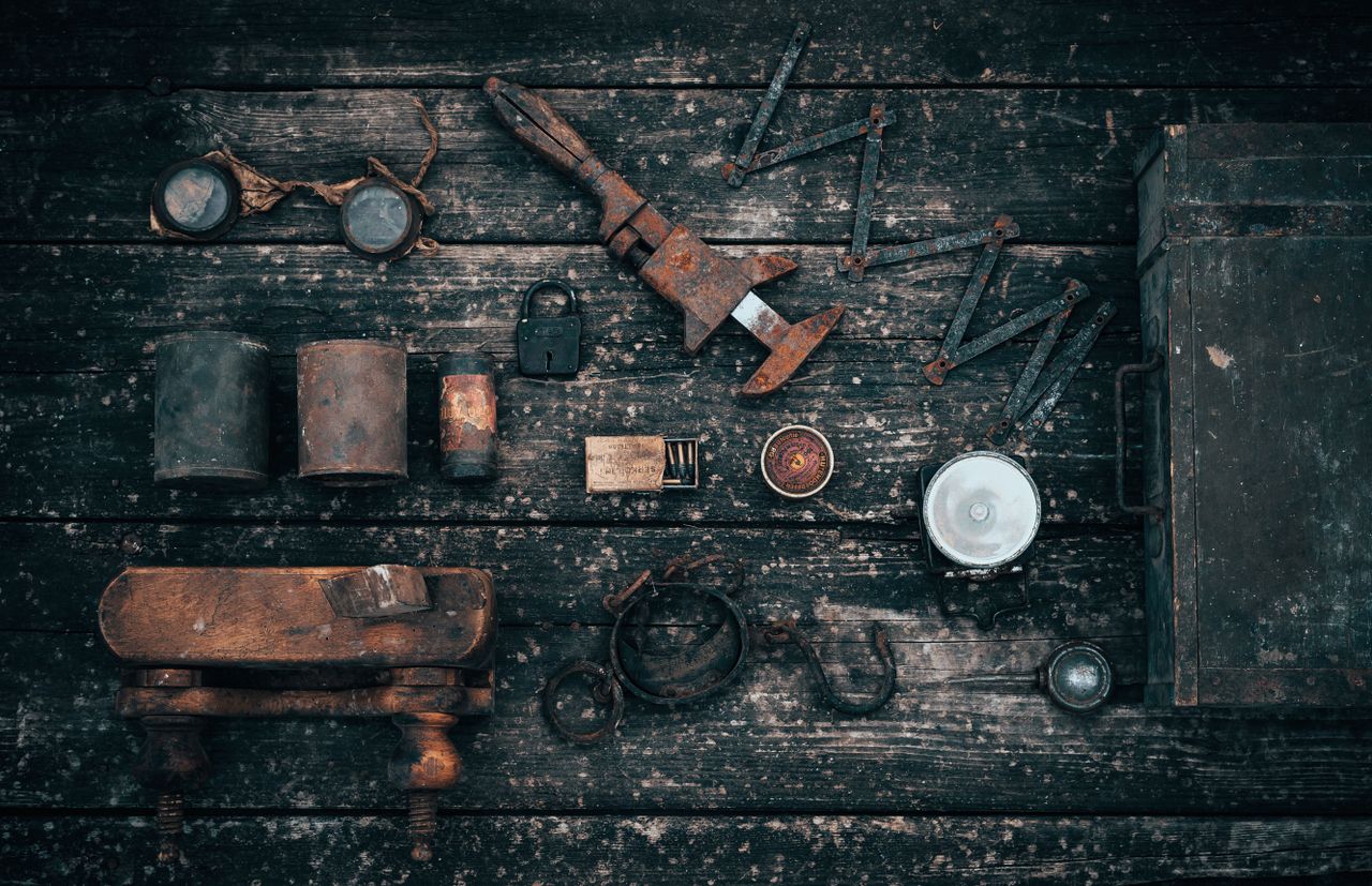 Top view of various old carpentry tools and tin cans arranged on shabby wooden table in garage
